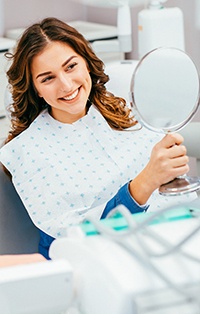 Young female dental patient examining smile in mirror